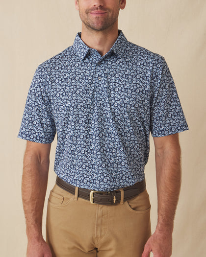 Men's Don Ho Polo in New Indigo, front view on model featuring a navy base with an all-over light blue floral print, paired with khaki pants and a dark leather belt