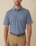 Men's Don Ho Polo in New Indigo, front view on model featuring a navy base with an all-over light blue floral print, paired with khaki pants and a dark leather belt