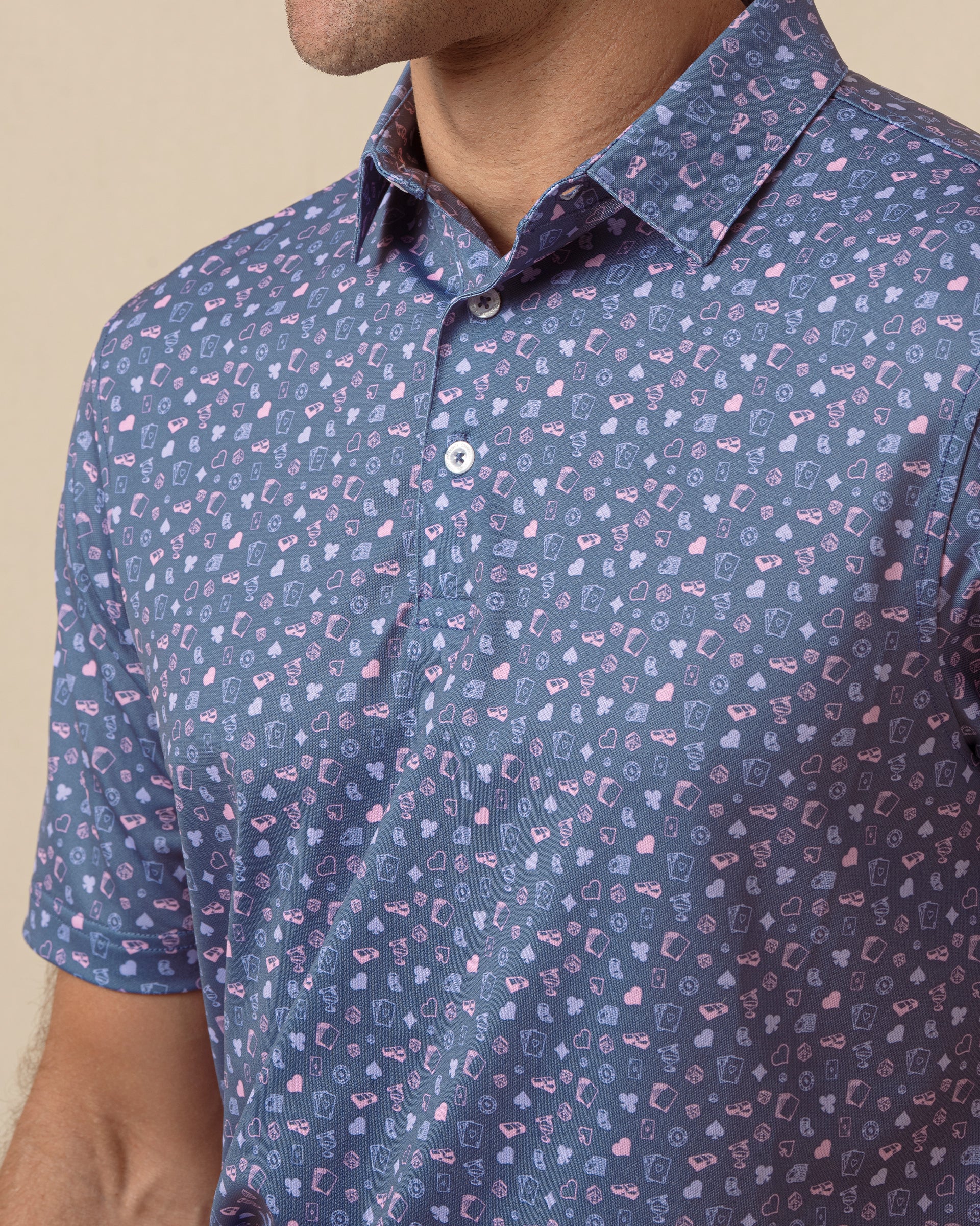 Close-up of blue polo with small playing card–inspired print in pink and light blue, featuring a button placket and structured collar