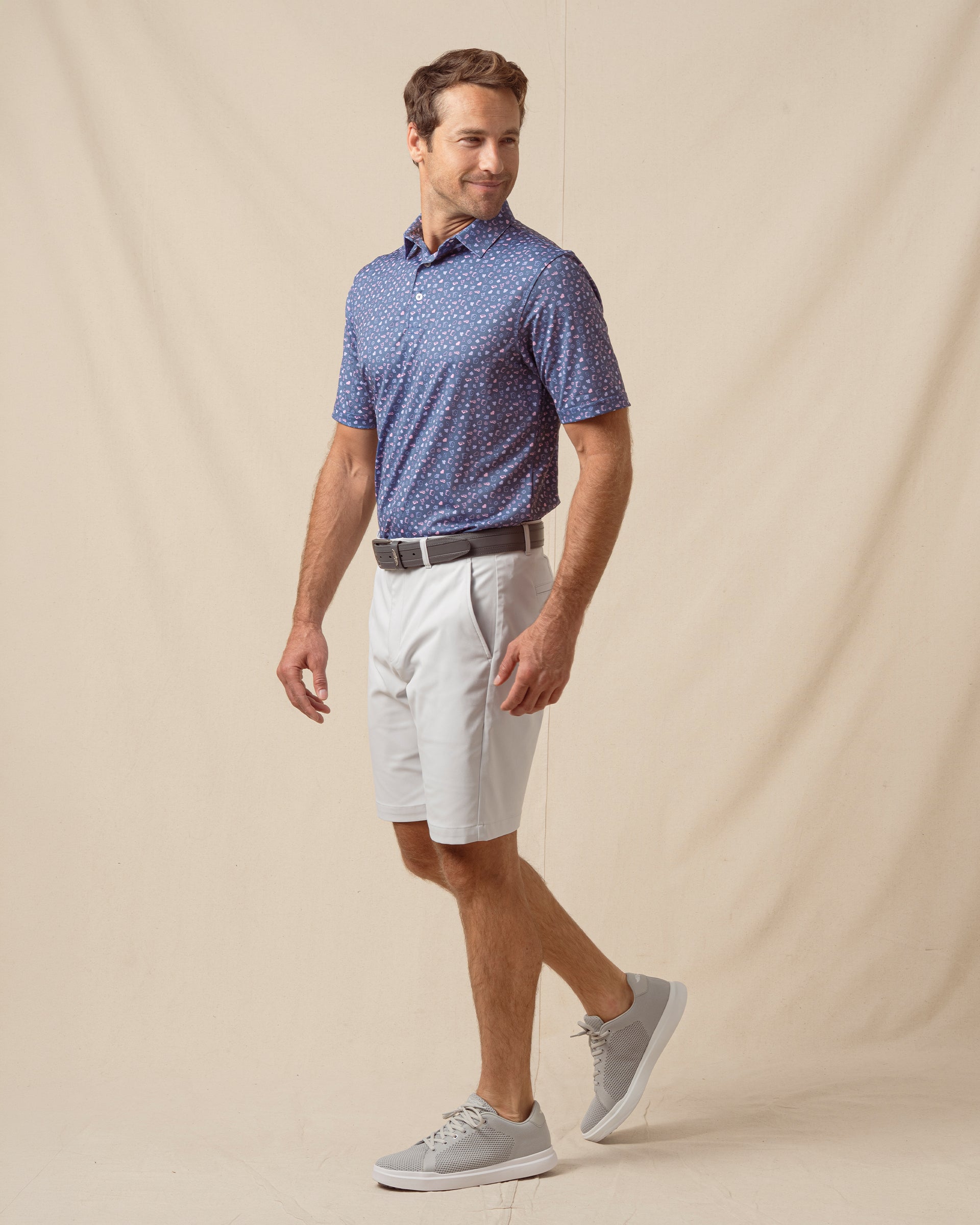 Men’s blue printed polo with card motif styled with light gray shorts, gray belt, and gray sneakers