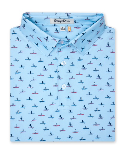 Men's Dog Paddle Polo in Cool Blue, folded flat lay front view featuring an all-over print of dogs paddle boarding on red and blue boards on a light blue body with a two-button placket and Straight Down label