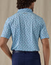Men's Dog Paddle Polo in Cool Blue, back view on model featuring an all-over print of dogs paddle boarding on red and blue boards on a light blue body with the Straight Down logo embroidered at the upper back, worn with navy pants