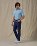 Men's Dog Paddle Polo in Cool Blue, full front view on model featuring an all-over print of dogs paddle boarding on red and blue boards on a light blue body, worn with navy pants, a navy belt, and white golf shoes