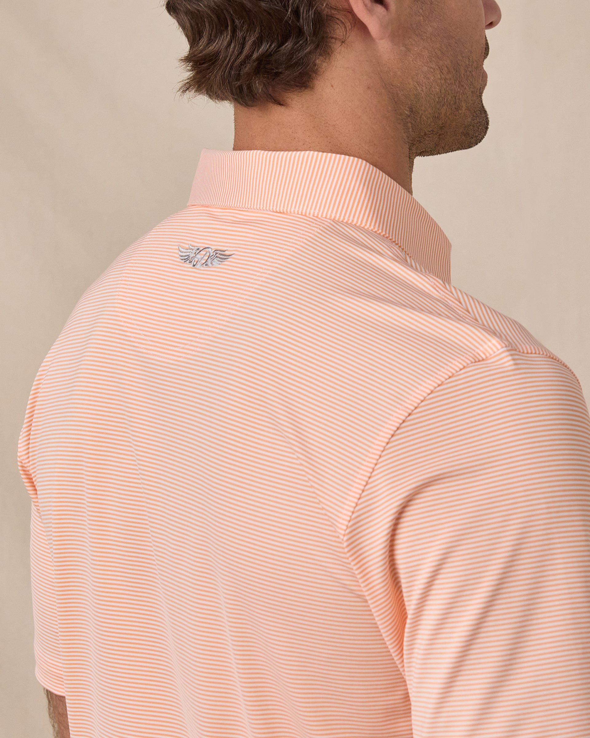 Men's Peninsula Stripe Polo in Cantalope, close-up back view on model, fine horizontal stripe fabric and Straight Down woven label at the sleeve hem