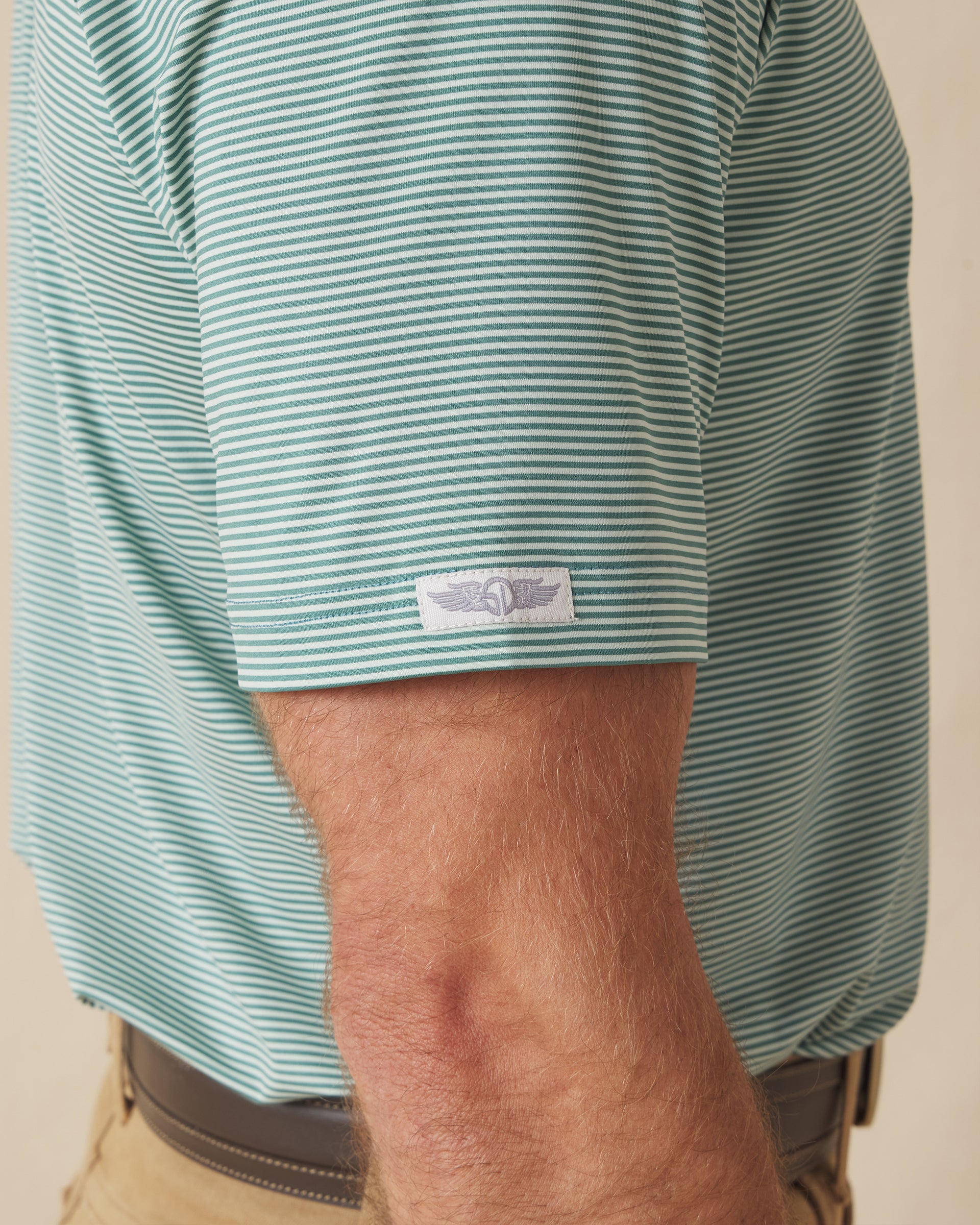 Men's Peninsula Stripe Polo in Celery, close-up detail view on model featuring Straight Down logo sleeve tab on green and white micro stripe pattern