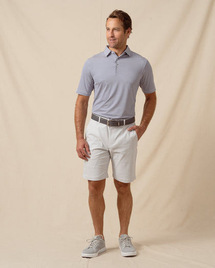 Men’s navy and white striped performance polo styled with light gray shorts and casual sneakers