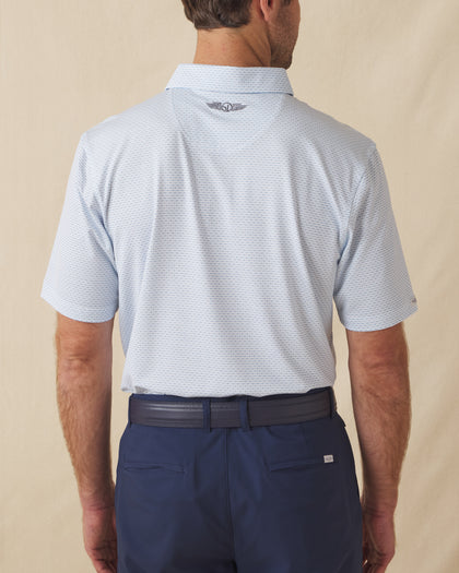 Men's Wilshire Polo in Gemstone, back view on model featuring a white base with an all-over blue geometric micro print, with Straight Down logo embroidered at upper back, paired with navy pants