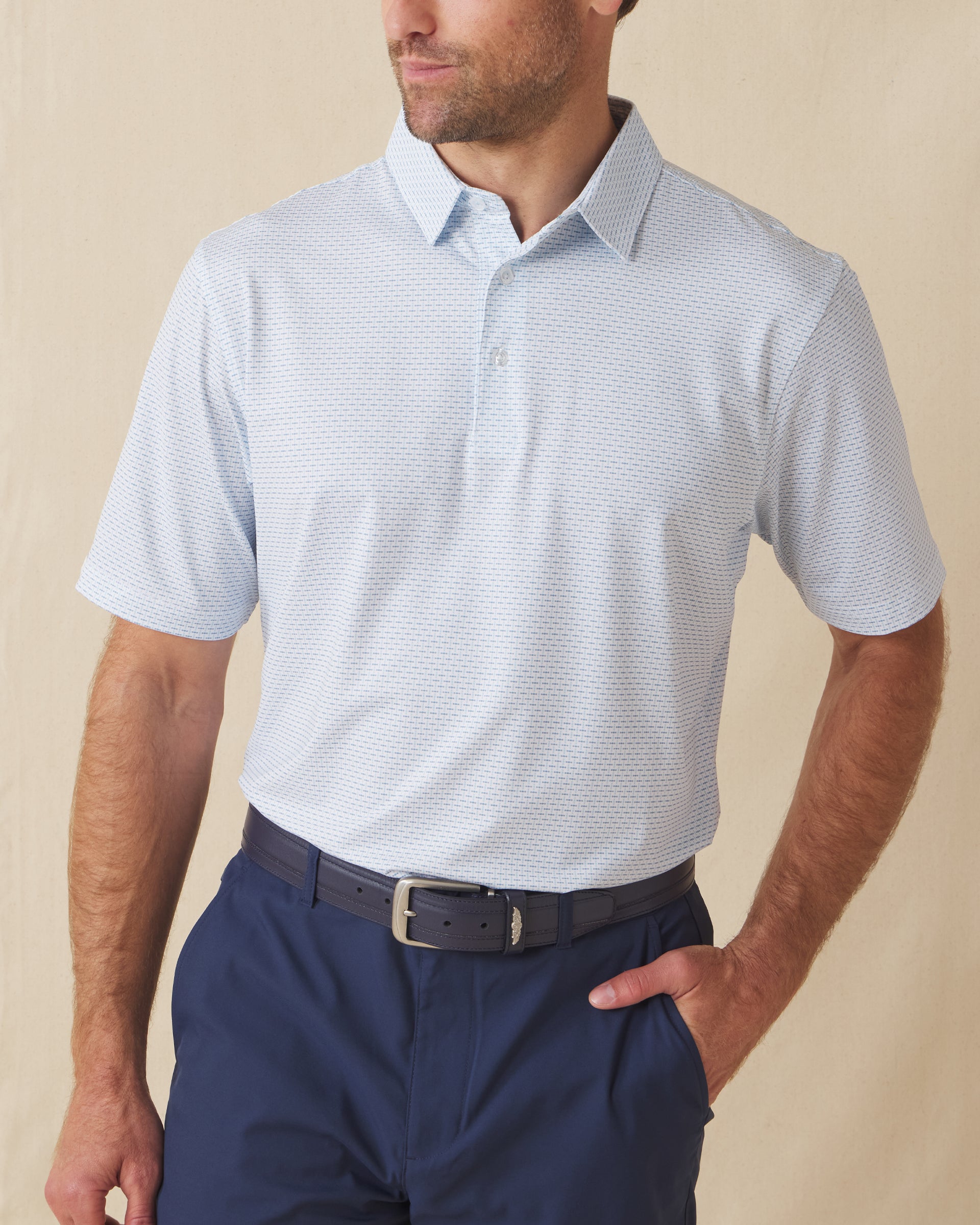 Men's Wilshire Polo in Gemstone, front view on model featuring a white base with an all-over blue geometric micro print, paired with navy pants and a dark leather belt