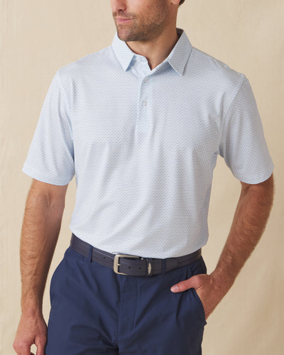 Men's Wilshire Polo in Gemstone, front view on model featuring a white base with an all-over blue geometric micro print, paired with navy pants and a dark leather belt
