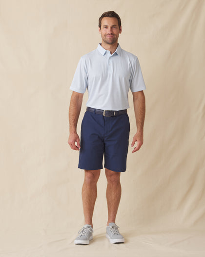 Men's Wilshire Polo in Gemstone, full length front view on model featuring a white base with an all-over blue geometric micro print, paired with navy shorts, a dark leather belt, and gray shoes