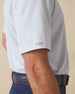 Men's Wilshire Polo in Gemstone, close-up sleeve view on model highlighting the Straight Down logo patch on the sleeve hem and the all-over blue geometric micro print on a white base