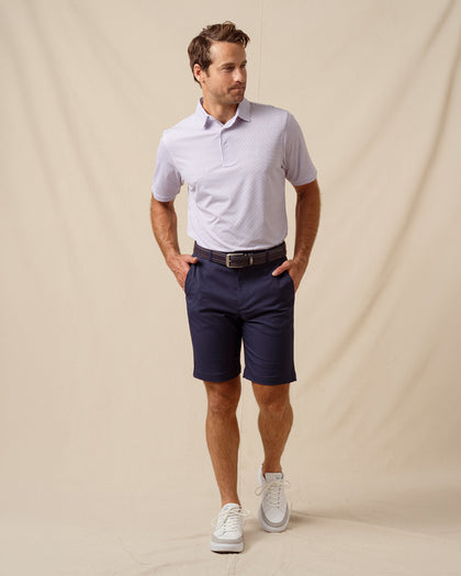 Men’s polo with two-tone geometric print in haze, styled with navy shorts, brown belt, and white sneakers