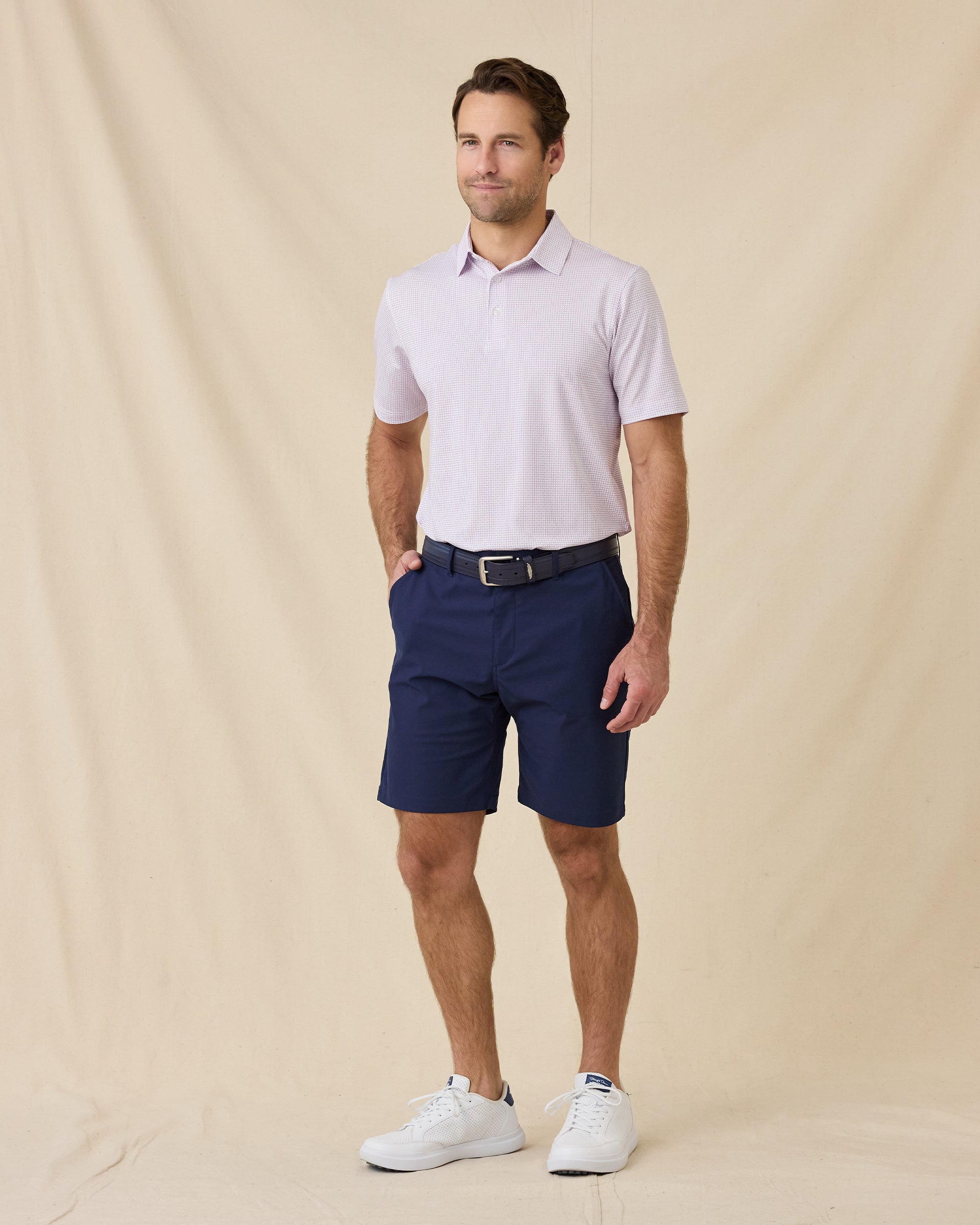 Model wearing the Wilshire Polo in Punch paired with navy golf shorts and white golf shoes