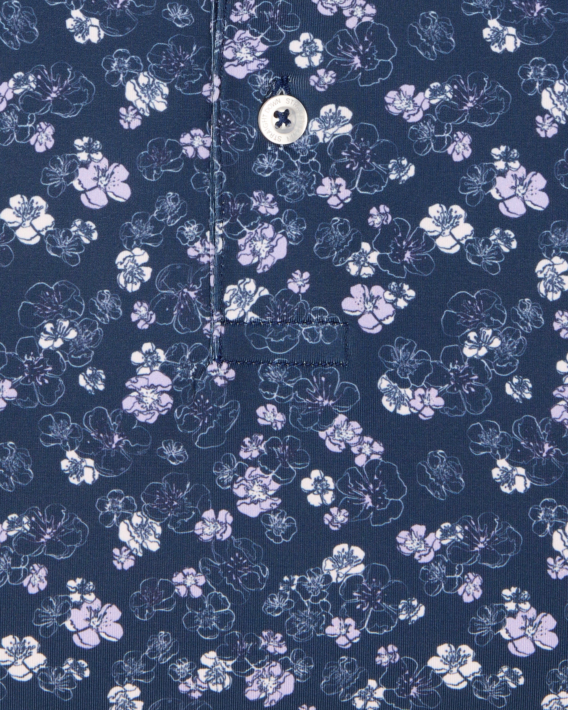 Men's Dogwood Polo in New Indigo, close-up flat lay view featuring a navy fabric with an all-over scattered floral blossom print in lavender and white with a visible button placket and chest pocket detail