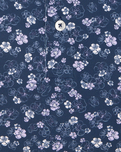 Men's Dogwood Polo in New Indigo, close-up flat lay view featuring a navy fabric with an all-over scattered floral blossom print in lavender and white with a visible button placket and chest pocket detail