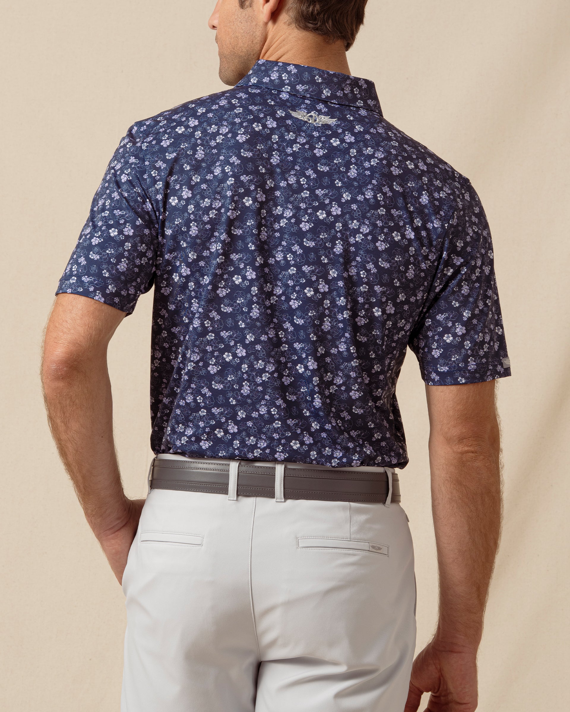 Back view of men’s navy floral print polo with allover pattern, paired with light gray shorts