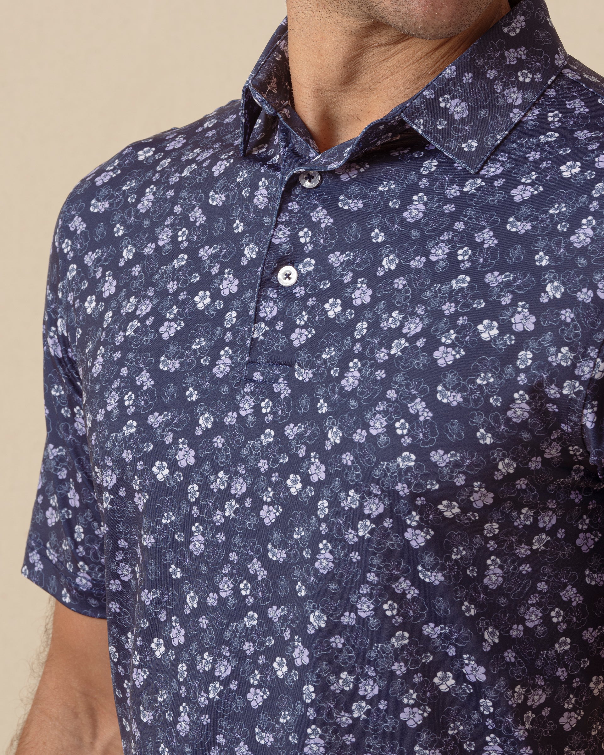 Close-up of navy polo shirt featuring small white floral print, button placket, and structured collar