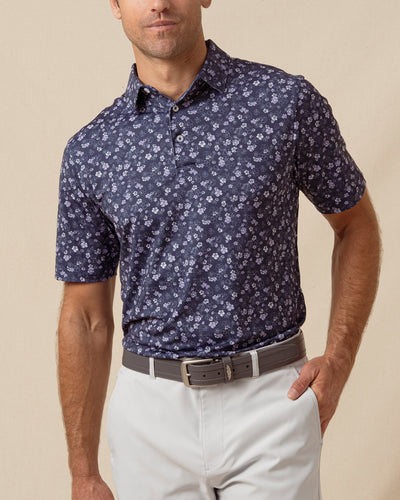 Men’s navy polo with allover floral print, styled with light gray shorts and a belt