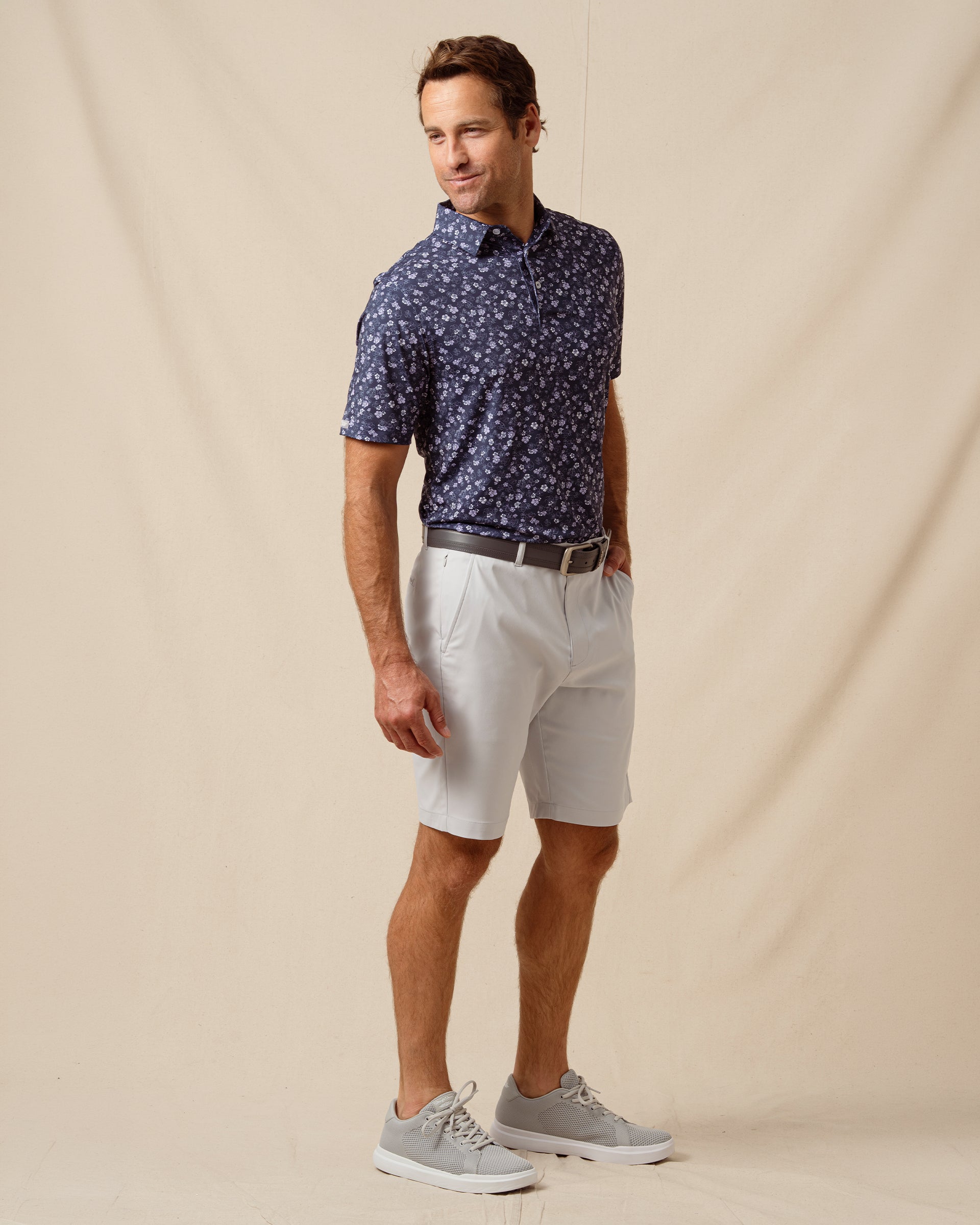 Men’s navy floral print polo shirt paired with light gray shorts, belt, and gray sneakers