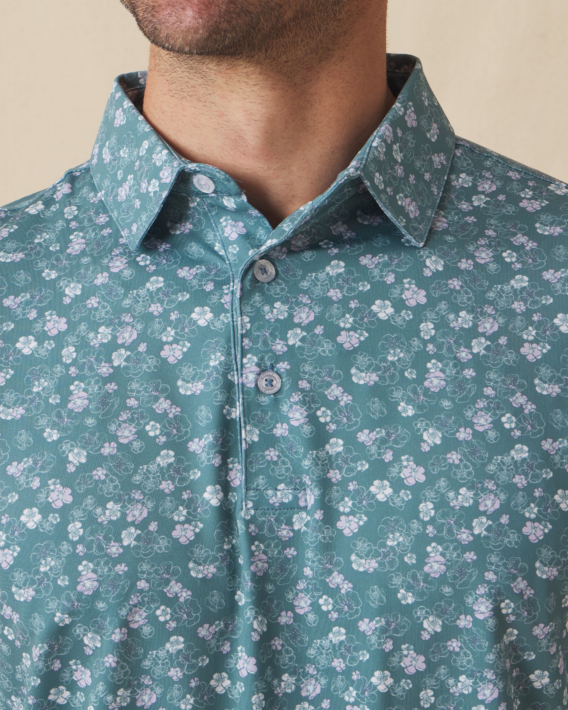 Men's Dogwood Polo in Sage, close-up detail view on model featuring a sage green base with scattered white and lavender floral print and spread collar