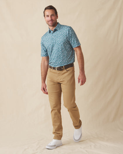 Men's Dogwood Polo in Sage, full-length front view on model featuring a sage green base with a scattered white and lavender floral print, paired with khaki pants and white golf shoes