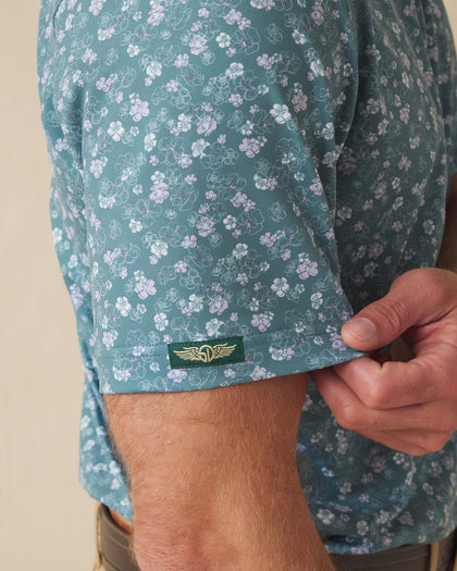 Men's Dogwood Polo in Sage, close-up detail view on model featuring Straight Down logo sleeve tab on sage green base with scattered white and lavender floral print