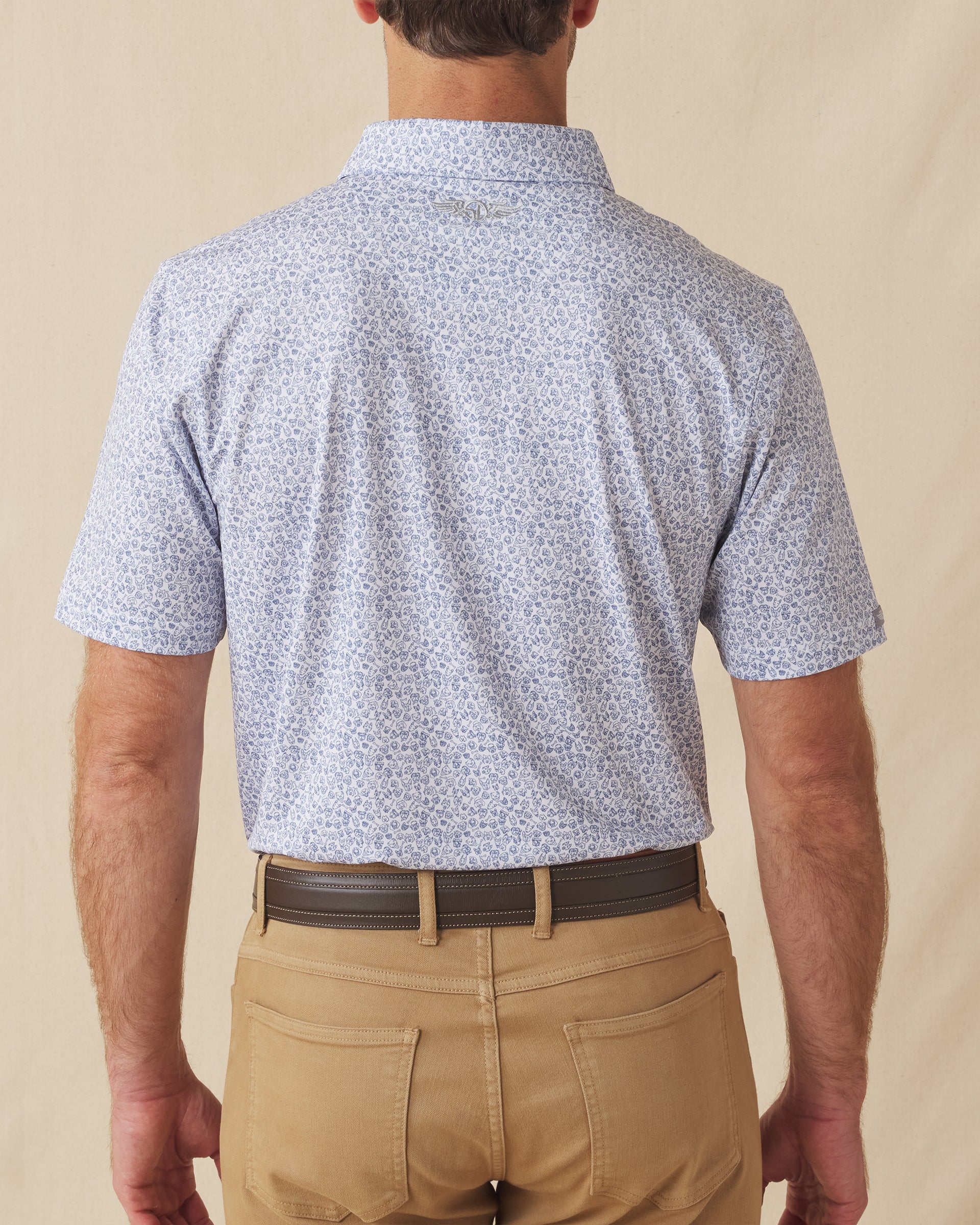 Men's Dog Pound Polo in Moonlight, back model view featuring a white short sleeve polo with an all-over scattered dog face and bone print in navy with the Straight Down logo at the back collar