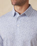 Men's Dog Pound Polo in Moonlight, close-up model view featuring the collar and button placket detail of a white short sleeve polo with an all-over scattered dog face and bone print in navy
