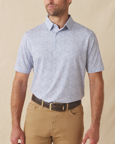 Men's Dog Pound Polo in Moonlight, front model view featuring a white short sleeve polo with an all-over scattered dog face and bone print in navy paired with khaki pants and a brown belt