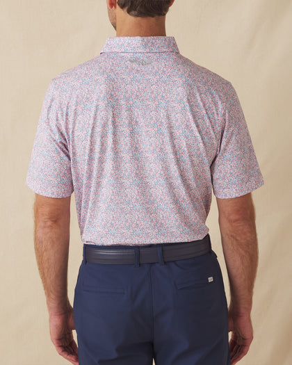 Men's Ocala Polo in Spritz, back view on model featuring a blue base with an all-over pink floral print, with Straight Down logo embroidered at upper back, paired with navy pants