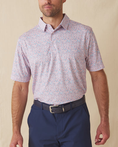Men's Ocala Polo in Spritz, front view on model featuring a blue base with an all-over pink floral print, paired with navy pants and a dark leather belt