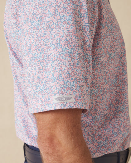 Men's Ocala Polo in Spritz, close-up sleeve view on model highlighting the Straight Down logo patch on the sleeve hem and the all-over pink floral print on a blue base