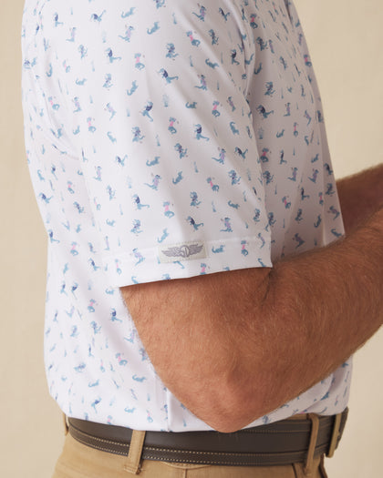Men's Gators Polo in Violet, close-up model view featuring the sleeve hem with the Straight Down logo tab detail on a white short sleeve polo with an all-over scattered golf-playing alligator print in blue and pink