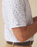 Men's Gators Polo in Violet, close-up model view featuring the sleeve hem with the Straight Down logo tab detail on a white short sleeve polo with an all-over scattered golf-playing alligator print in blue and pink