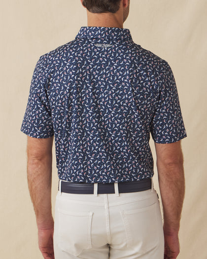 Men's Manatee County Polo in New Indigo, back model view featuring a navy short sleeve polo with an all-over scattered golf-playing manatee print in white and pink with the Straight Down logo at the back collar