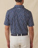 Men's Manatee County Polo in New Indigo, back model view featuring a navy short sleeve polo with an all-over scattered golf-playing manatee print in white and pink with the Straight Down logo at the back collar