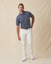 Men's Manatee County Polo in New Indigo, full length model view featuring a navy short sleeve polo with an all-over scattered golf-playing manatee print in white and pink paired with white pants and white shoes