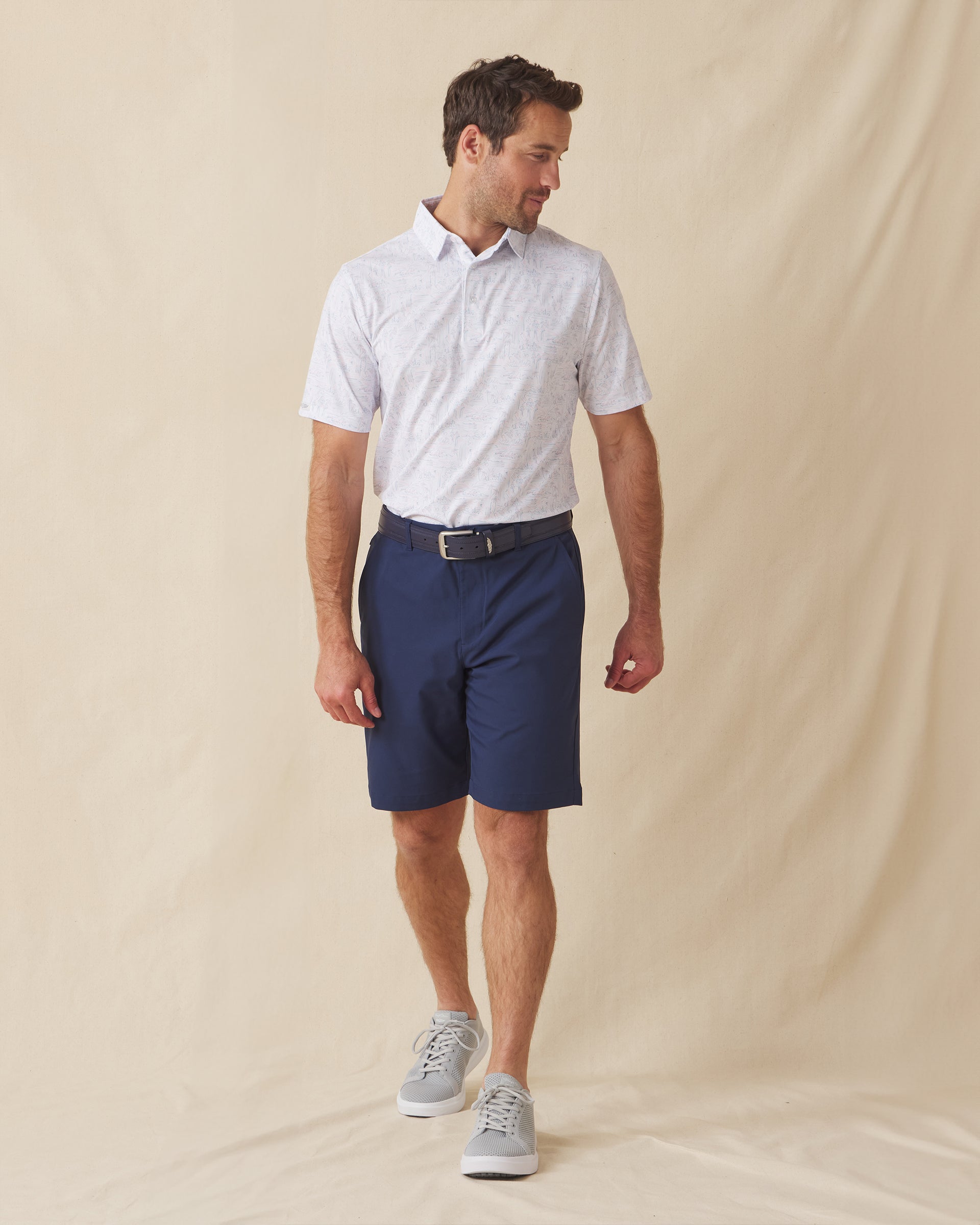 Men's Golden State Polo in Spritz, full length front view on model featuring a white base with an all-over blue and pink California landscape sketch print, paired with navy shorts, a dark leather belt, and gray shoes