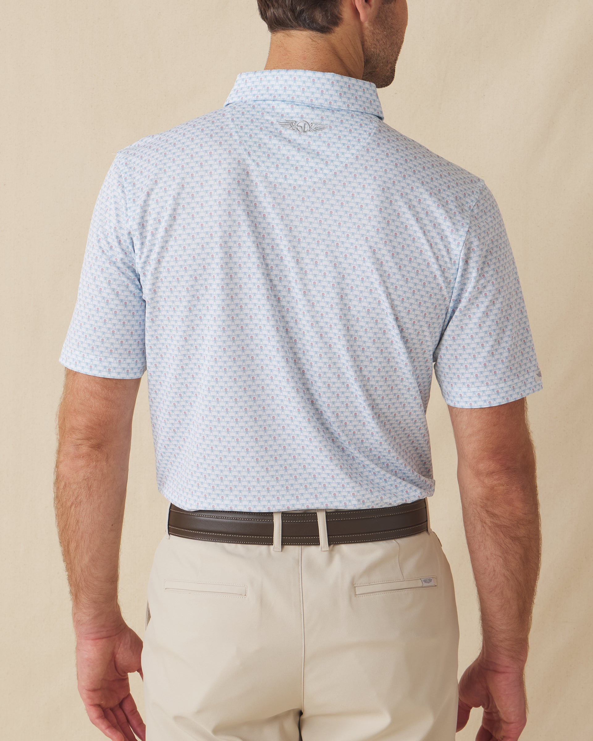 Men's Slam Dunk Polo in Coastal, back view on model featuring an allover basketball hoop and ball print in light blue and pink on white, with the Straight Down logo embroidered at center back, paired with khaki pants and a brown belt