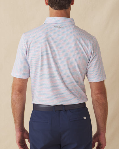 Men's Cocora Polo in Coastal, back view on model featuring a white base with an all-over blue and pink palm tree micro print, with Straight Down logo embroidered at upper back, paired with navy pants