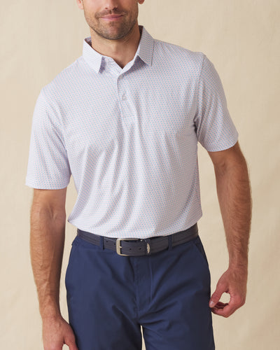 Men's Cocora Polo in Coastal, front view on model featuring a white base with an all-over blue and pink palm tree micro print, paired with navy pants and a dark leather belt