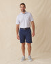 Men's Cocora Polo in Coastal, full length front view on model featuring a white base with an all-over blue and pink palm tree micro print, paired with navy shorts, a dark leather belt, and gray shoes