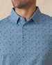Men's Tannins & Tees Polo in Coastal, close-up front view on model highlighting the scattered wine bottle, wine glass, barrel, and corkscrew print in navy on a blue base