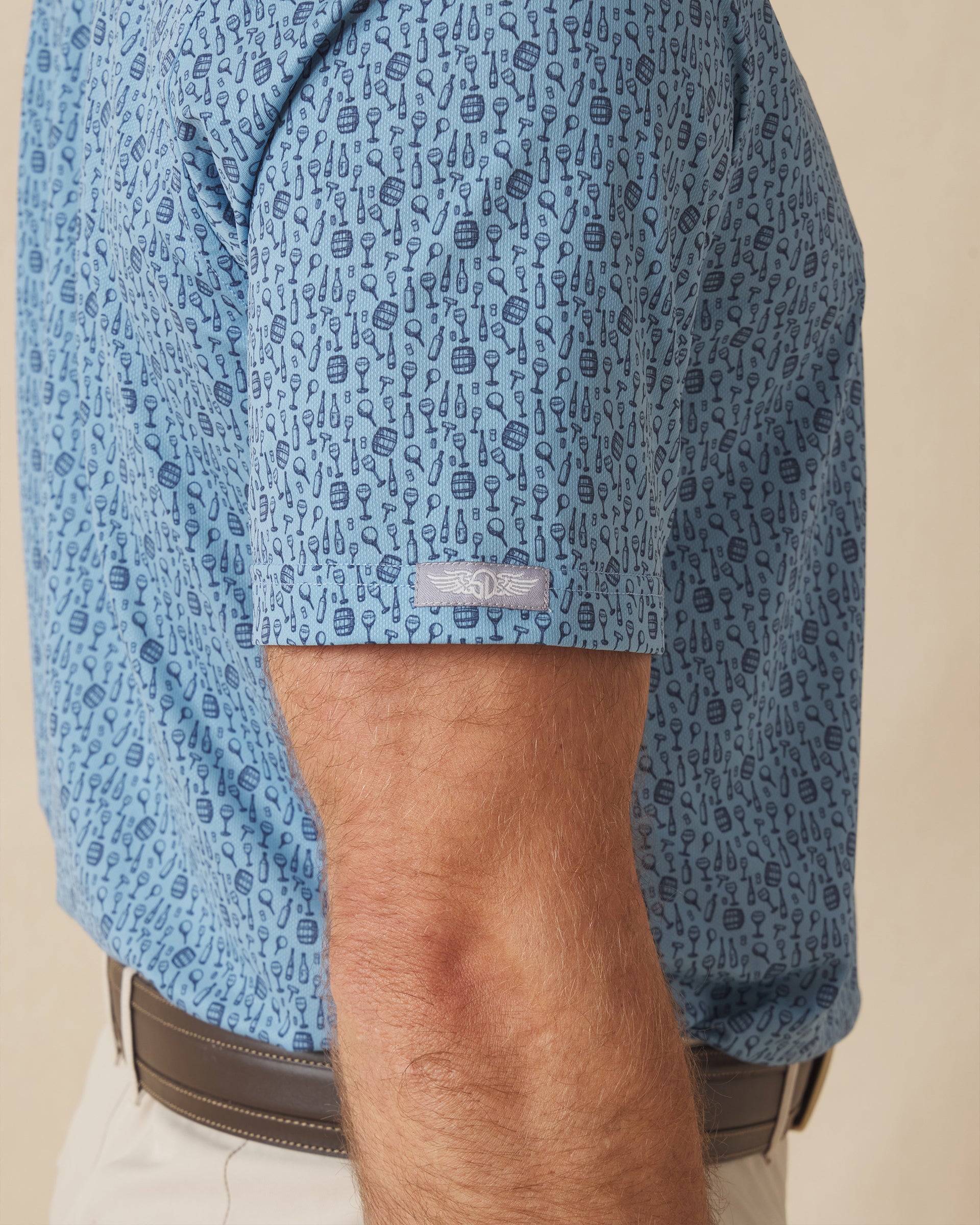 Men's Tannins & Tees Polo in Coastal, close-up sleeve view on model highlighting the Straight Down logo patch on the sleeve hem and the scattered wine print in navy on a blue base
