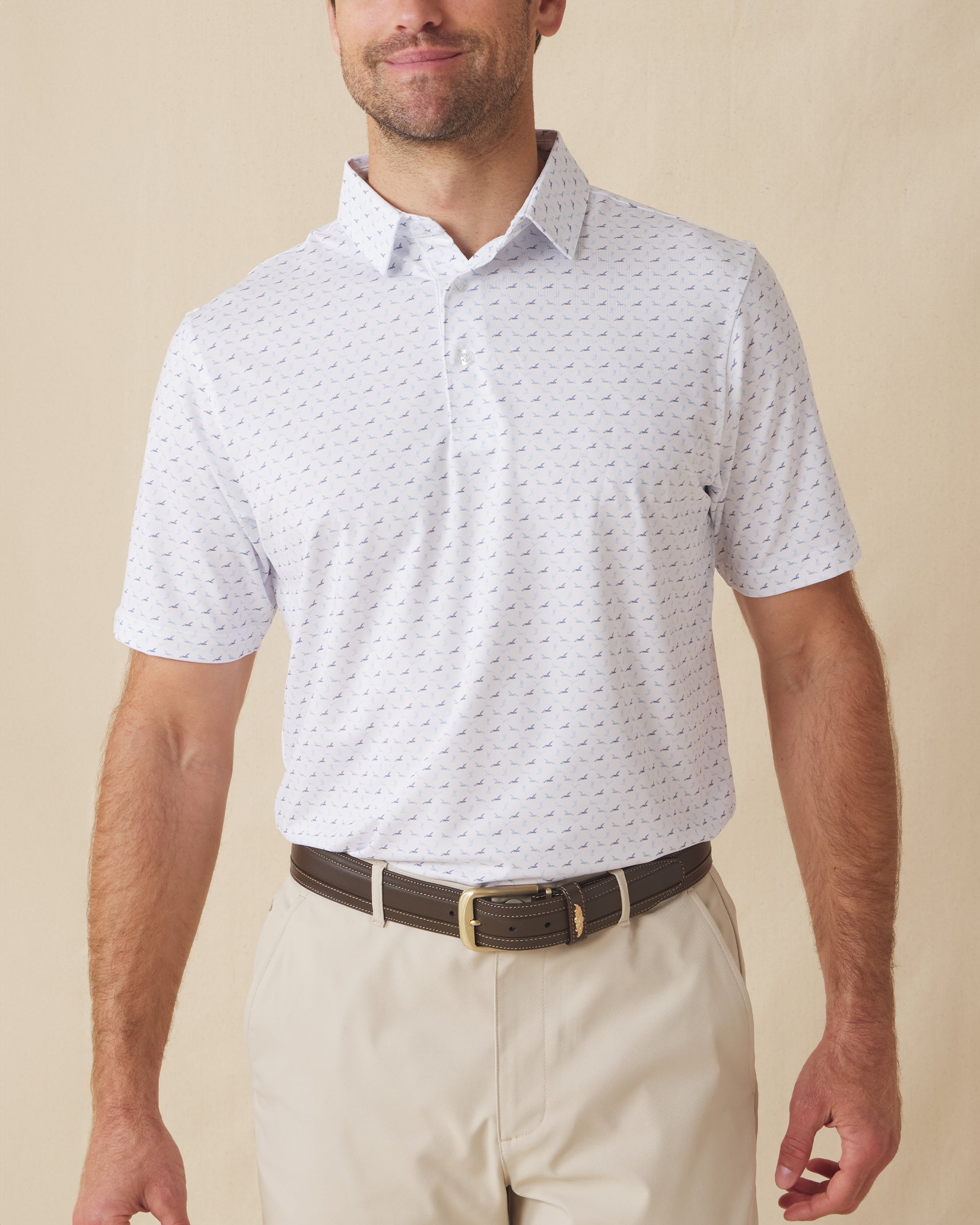 Men's Livingston Polo in White, front view on model featuring a white base with a scattered navy and light blue seagull print, paired with khaki pants and a dark leather belt
