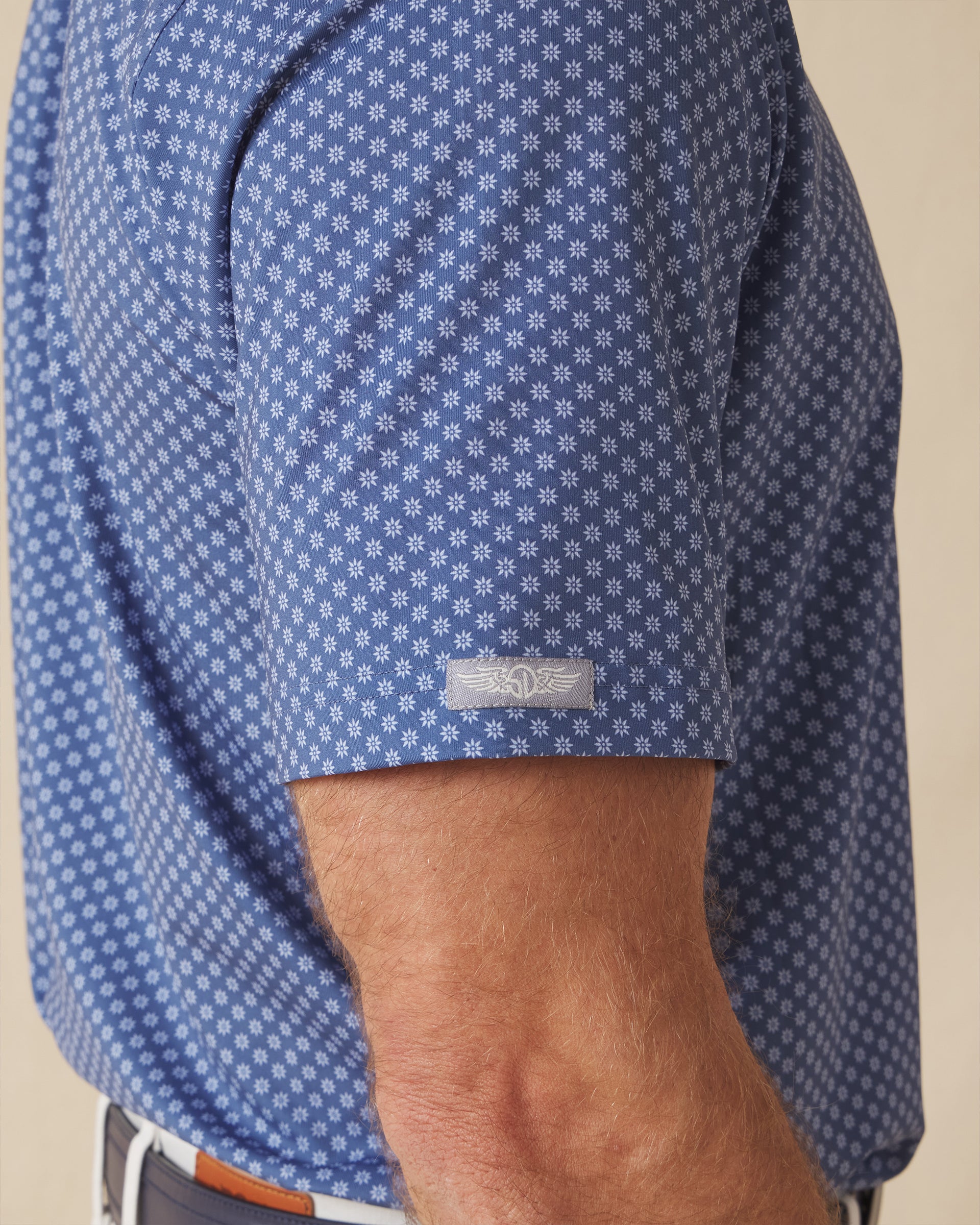 Close-up of polo sleeve with subtle logo tab and geometric floral pattern