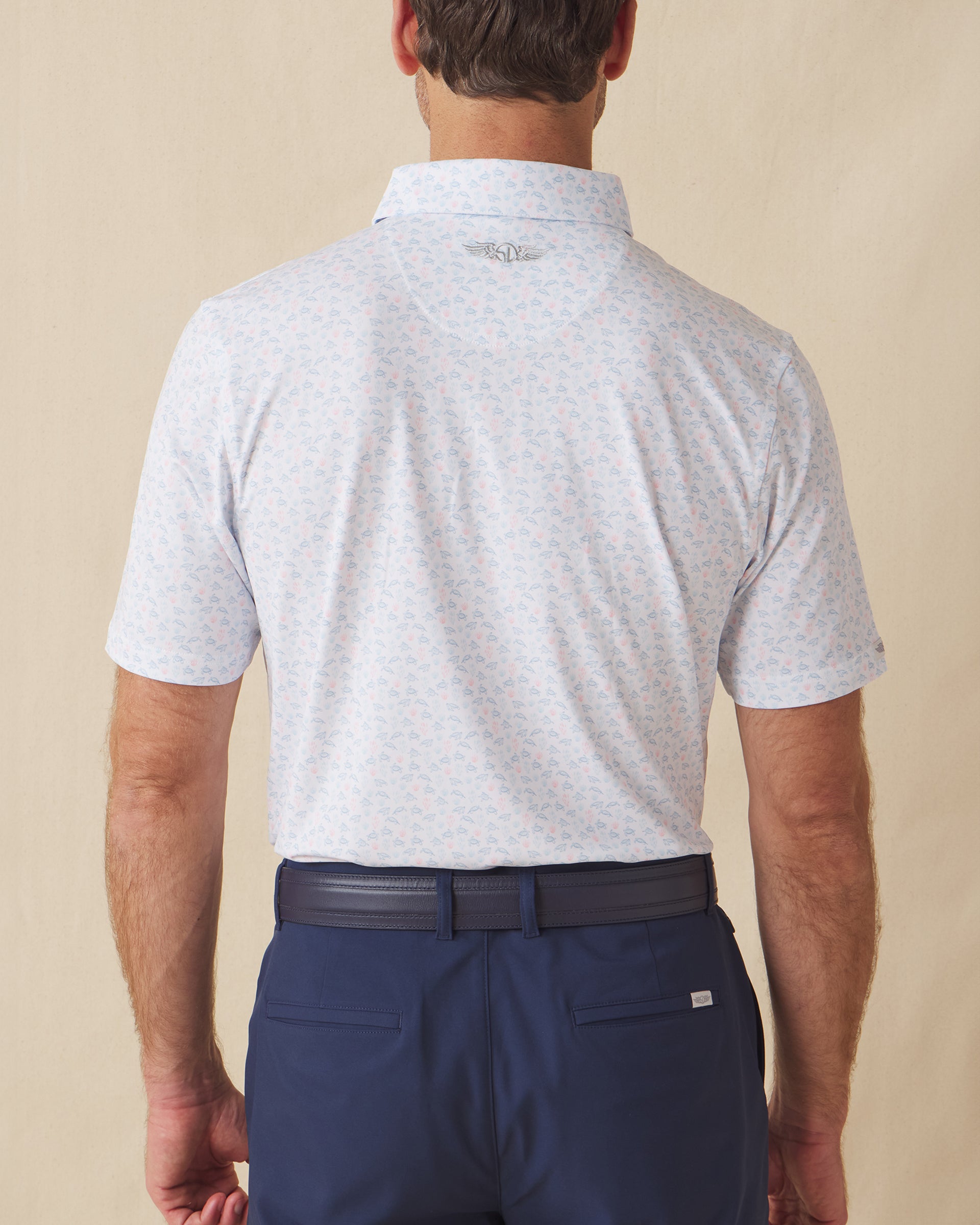 Men's Turtle Island Polo in Coastal, back model view featuring a white short sleeve polo with an allover sea turtle and coral print in light blue and pink tones, with a Straight Down logo at the back collar