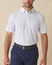 Men's Turtle Island Polo in Coastal, front model view featuring a white short sleeve polo with an allover sea turtle and coral print in light blue and pink tones, styled with navy shorts and a leather belt
