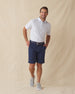 Men's Turtle Island Polo in Coastal, full length model view featuring a white short sleeve polo with an allover sea turtle and coral print in light blue and pink tones, styled with navy shorts and gray shoes