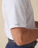 Men's Turtle Island Polo in Coastal, sleeve detail view featuring a white short sleeve polo with an allover sea turtle and coral print in light blue and pink tones, with a Straight Down logo tab on the sleeve hem